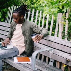 young student with coffee to go using laptop in park
