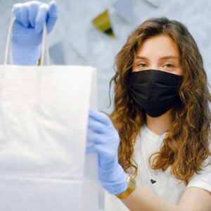 woman with face mask and latex gloves holding a shopping bag