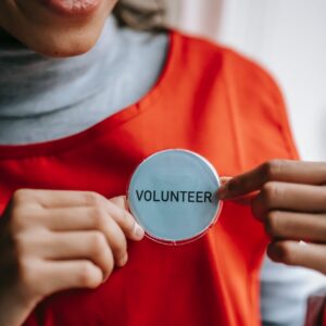 smiling ethnic woman showing volunteer sign on red apron
