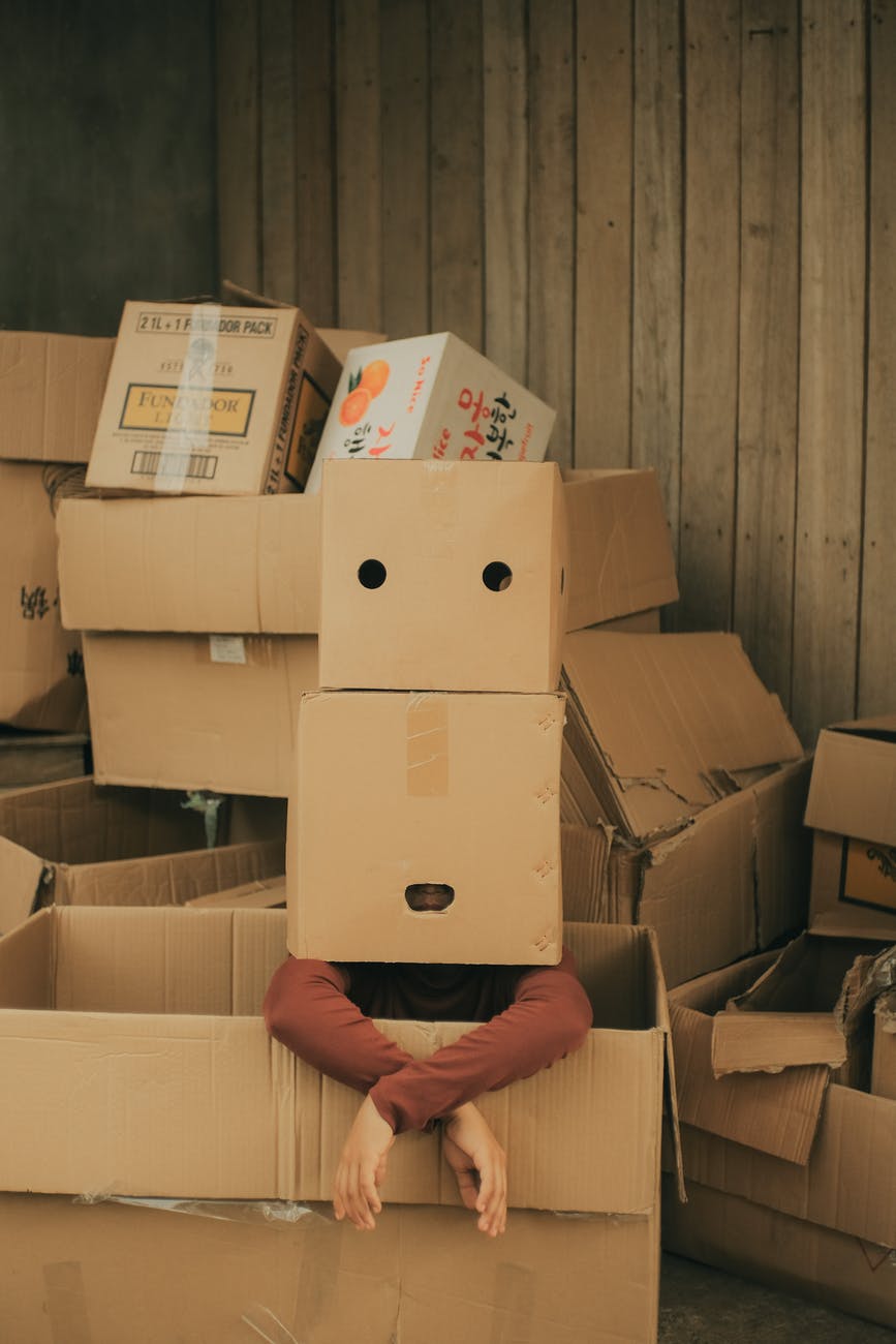 anonymous person with box on head near carton boxes