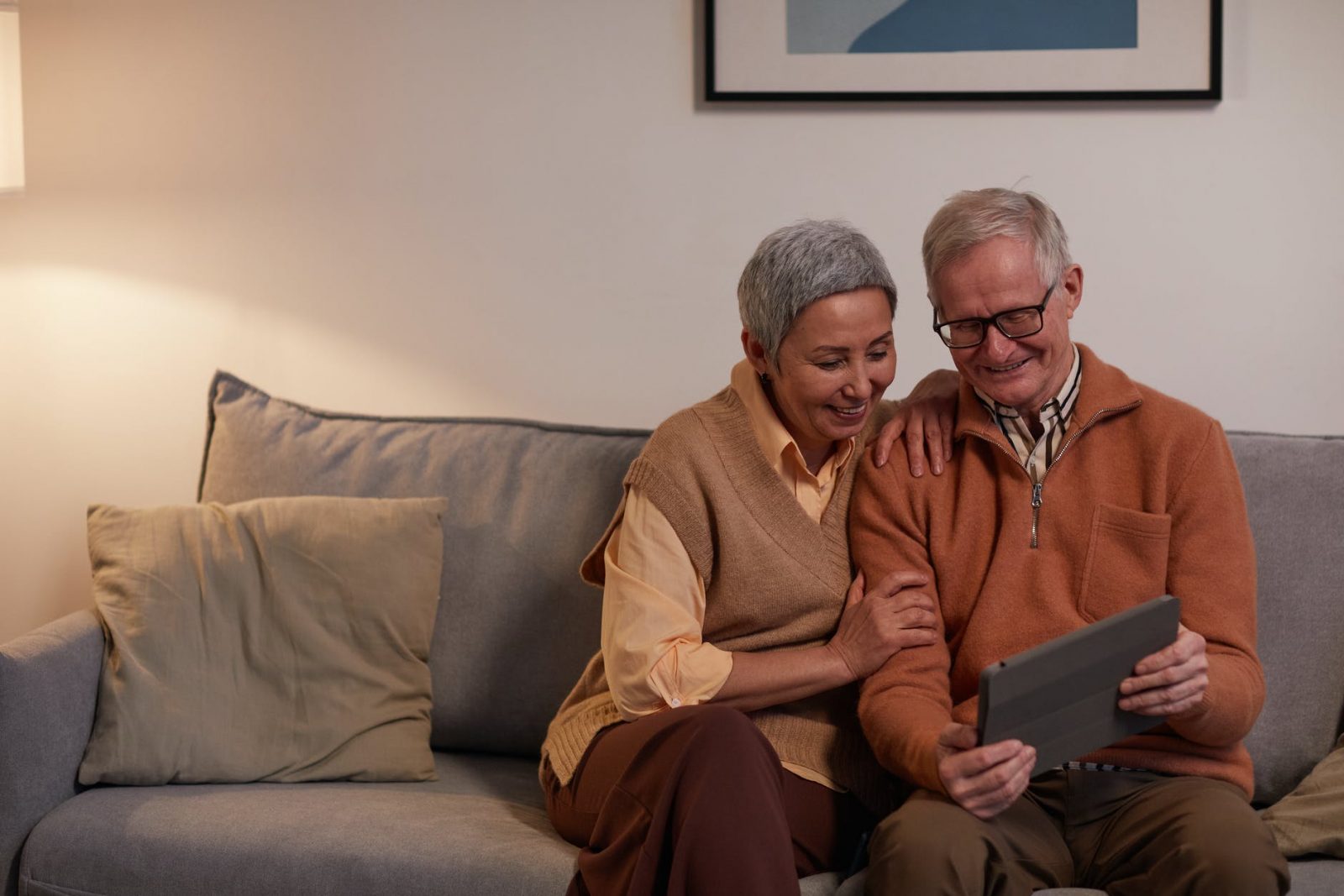 man and woman sitting on sofa while looking at a tablet computer