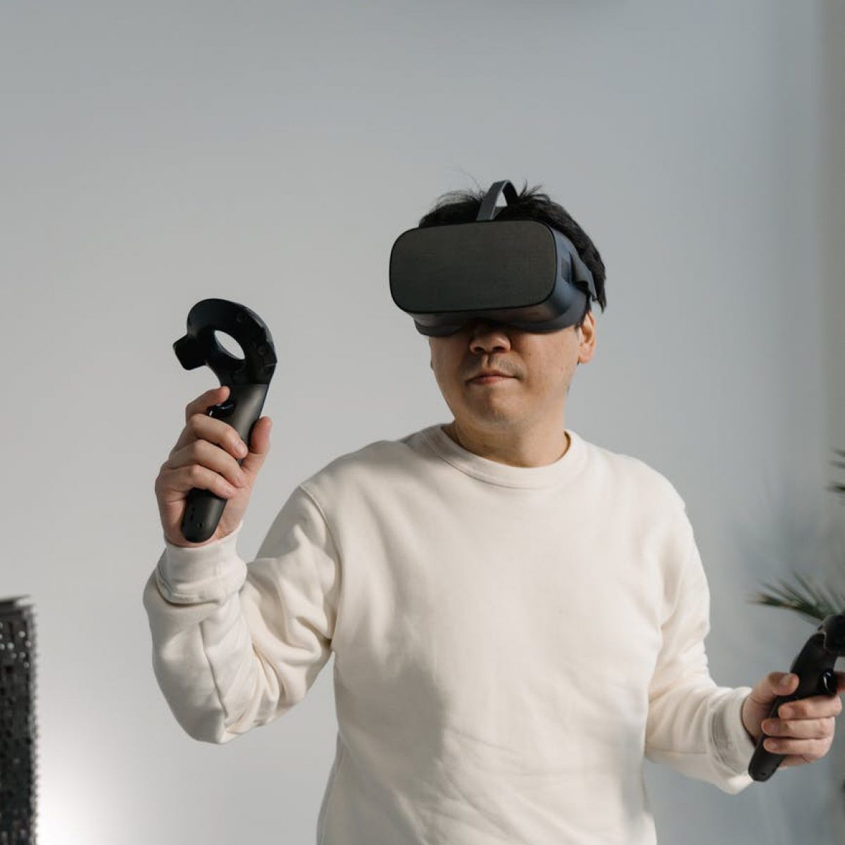 man in white sweatshirt wearing a virtual reality headset with game controllers