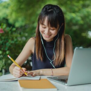 happy young asian student doing homework and listening to music with earphones