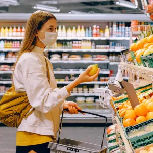 woman in yellow tshirt and beige jacket holding a fruit stand