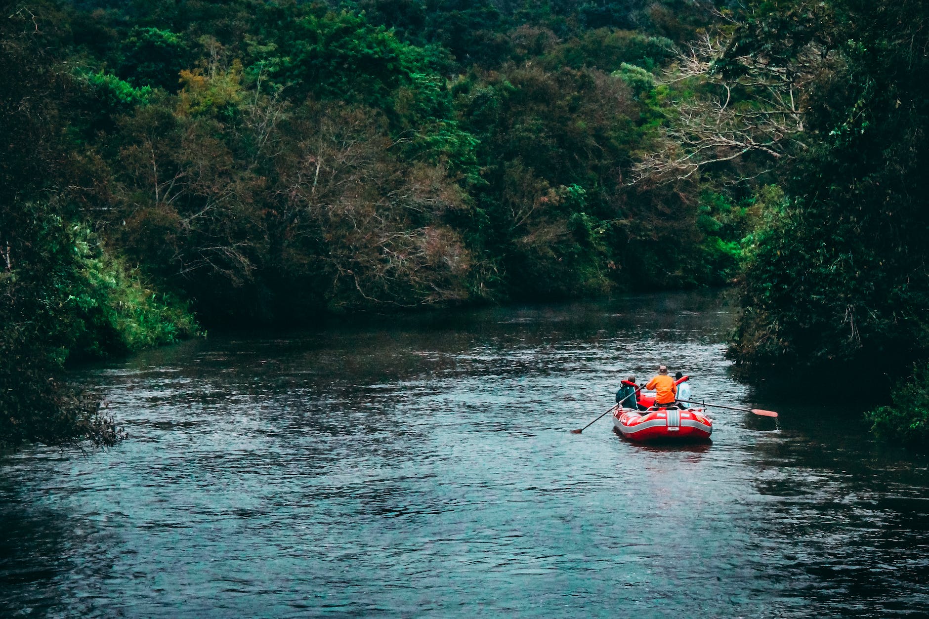 three persons riding red inflatable raft