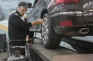 serious car mechanic pumping up car wheel in modern service garage