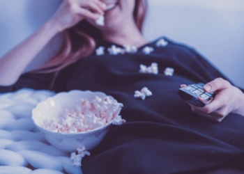 woman lying on bed while eating puff corn