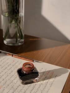 A Bottle of Ink and a Quill Lying on a Page with a Handwritten